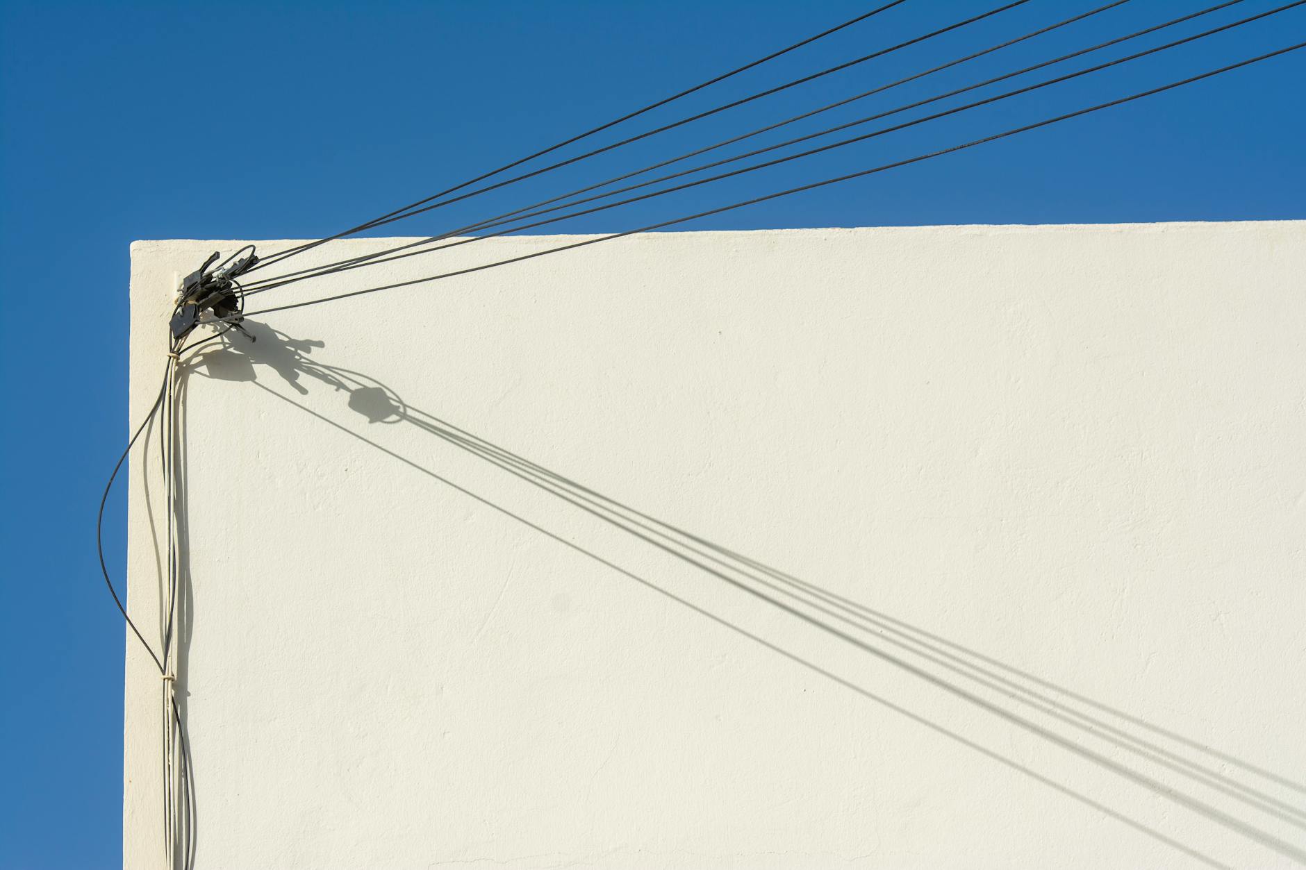 Cienie przewodów elektrycznych na białej ścianie na tle błękitnego nieba