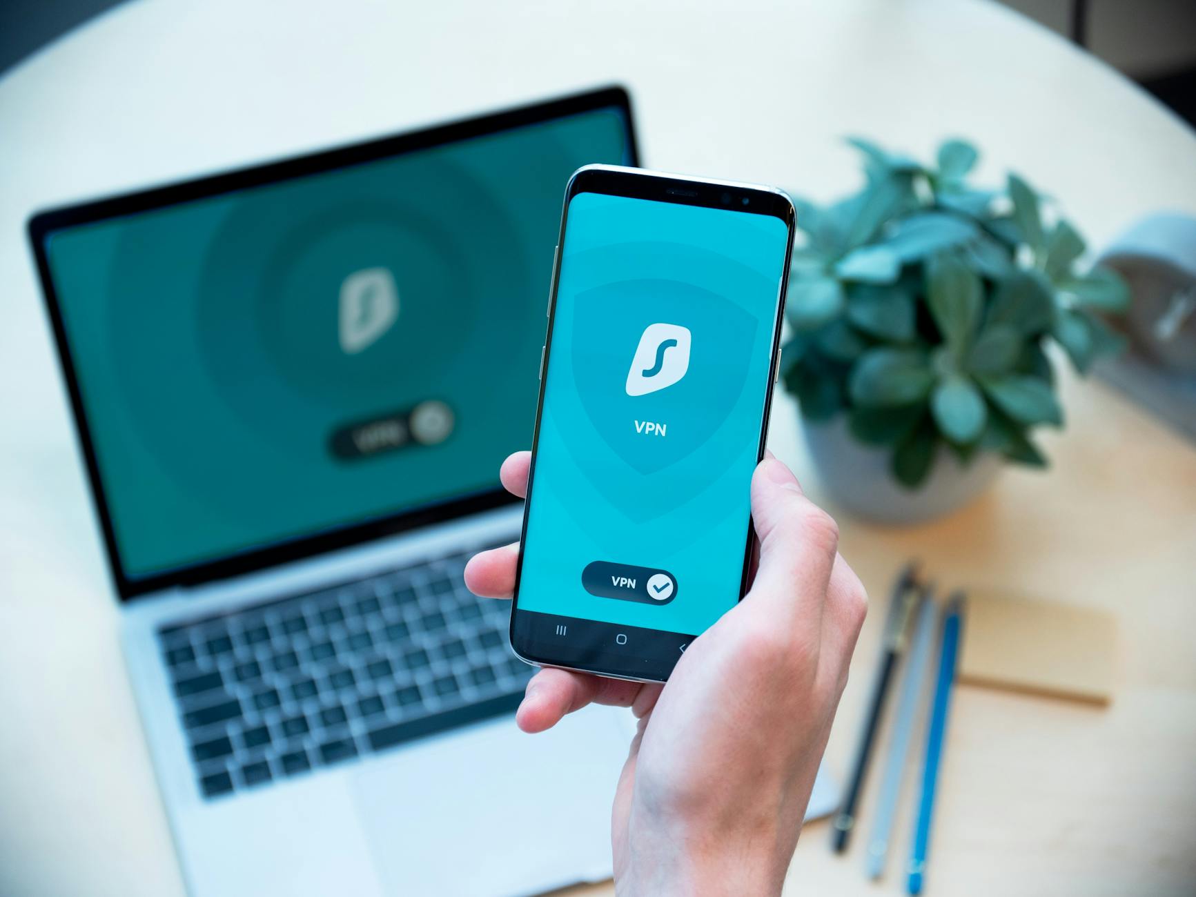 Dłoń trzymająca smartfon z aplikacją VPN na tle otwartego laptopa