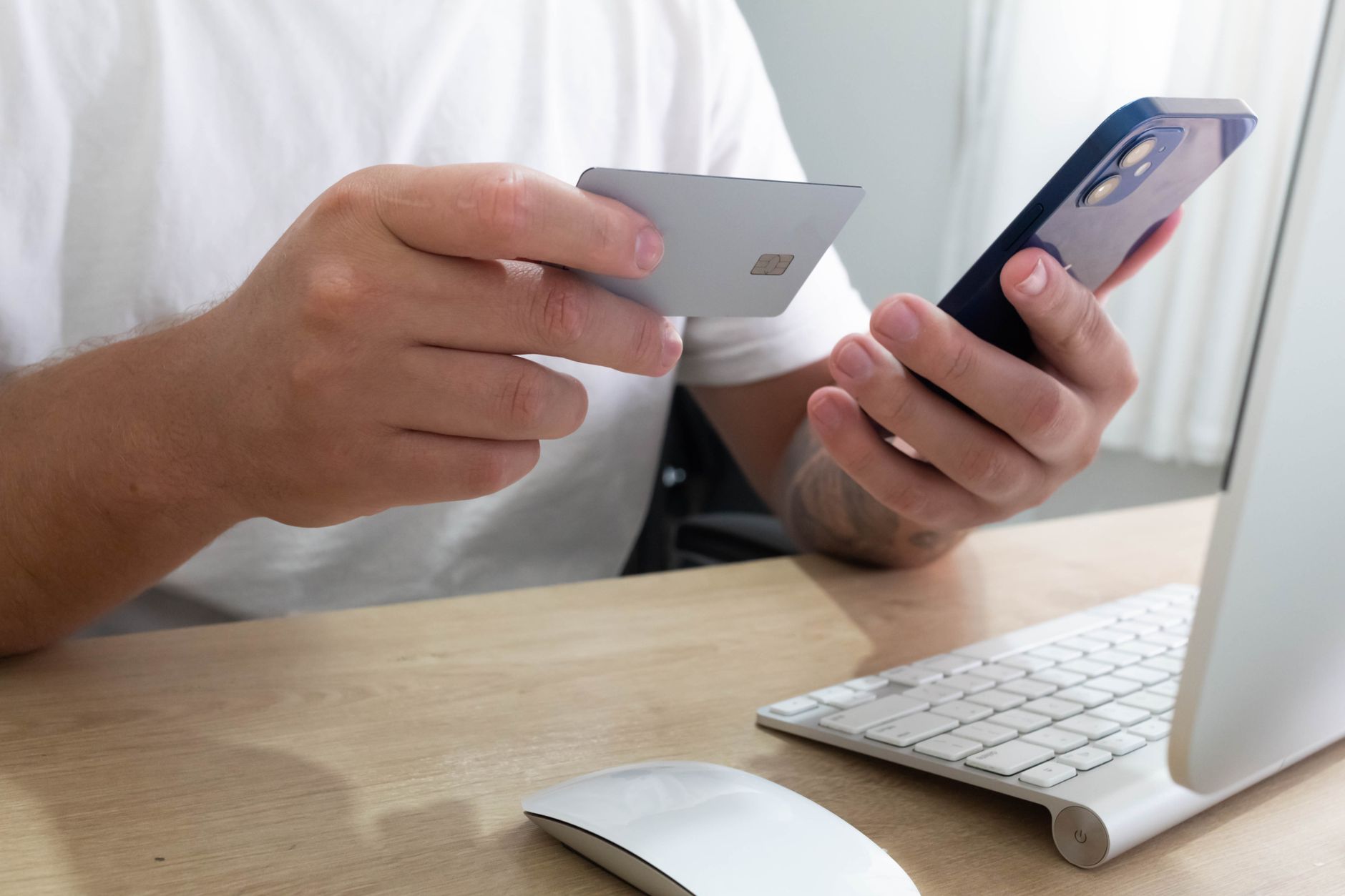 Osoba przy biurku trzymająca kartę płatniczą i smartfon podczas transakcji