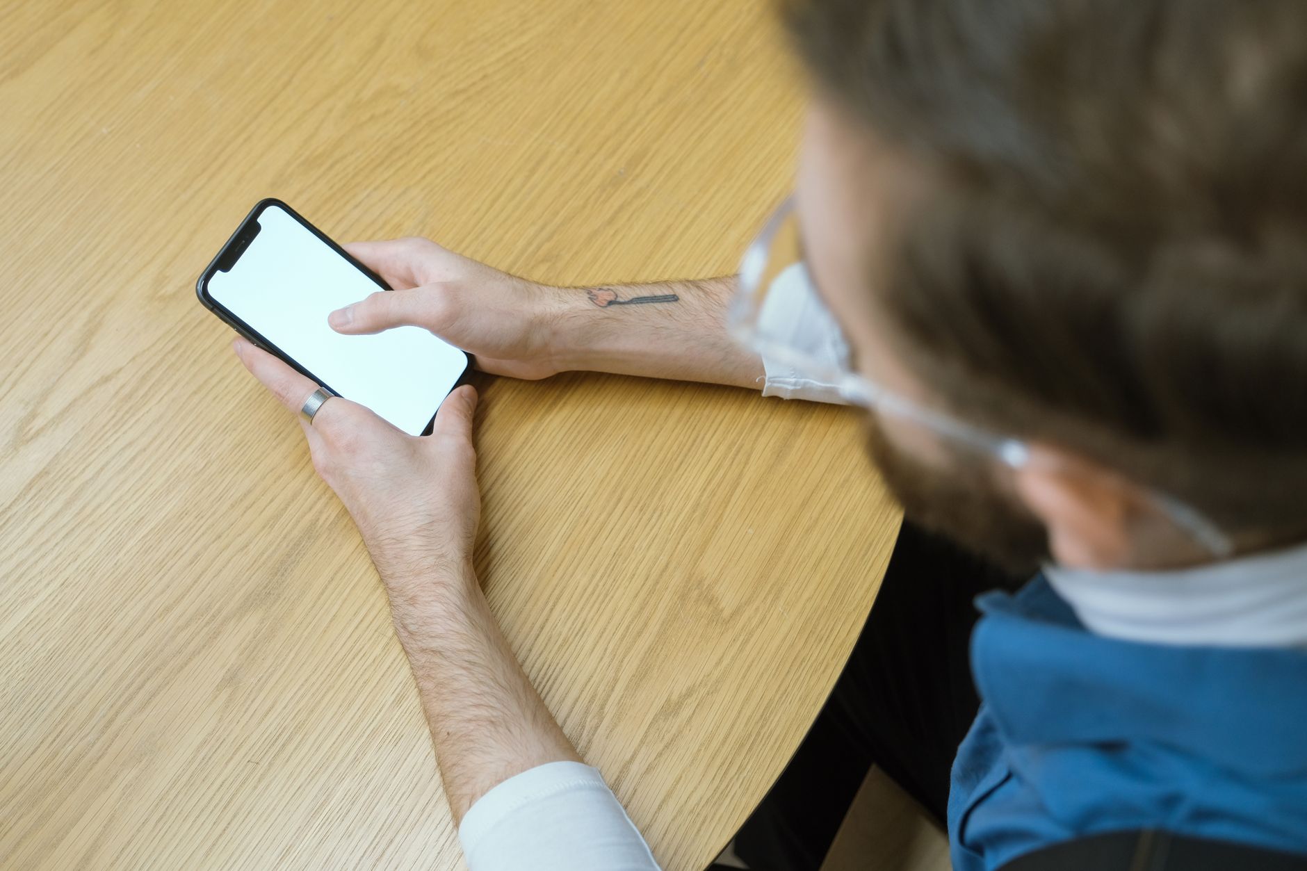 Osoba trzyma smartfon z pustym ekranem nad drewnianym stołem