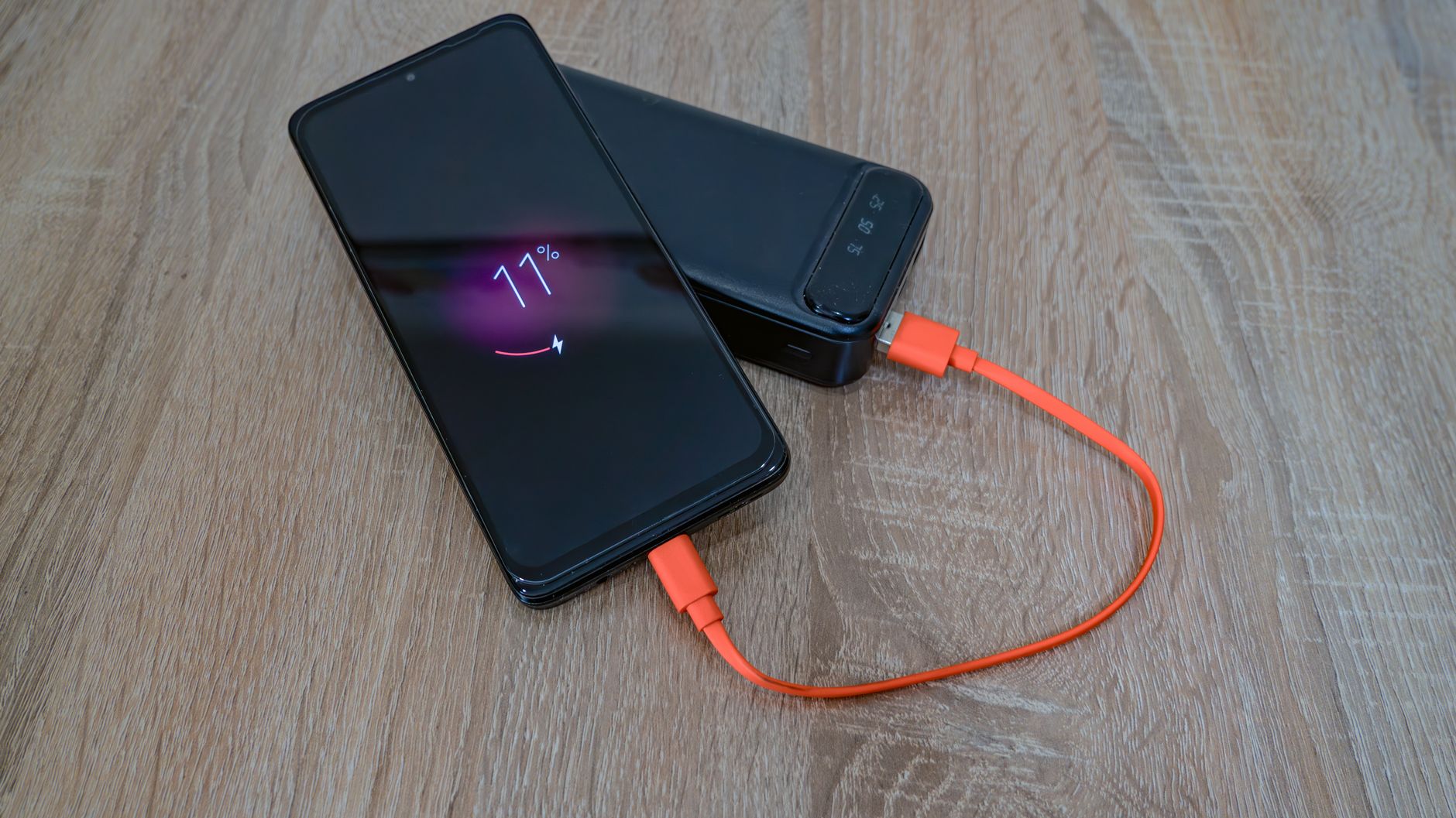 Smartfon ładowany powerbankiem kablem USB C na drewnianym stole